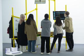 A group of people gathered in front of an exhibition piece with yellow bars