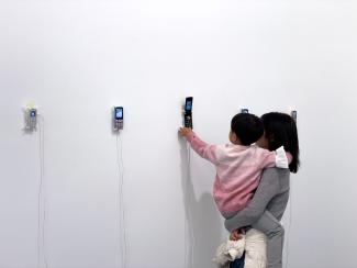 A baby in mother's arms reaching out to a phone suspended on the wall