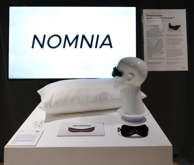 The logo stands bold against the void—NOMNIA. Framed by its curated environment, the installation draws viewers into its dream-economy fiction.